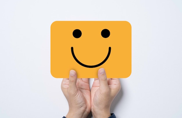 Hand holding and give yellow card with smile face for positive thinking mindset and excellent customer satisfaction and evaluation concept.