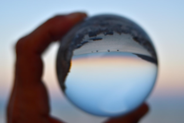 A hand holding a glass ball with the sky in the background.