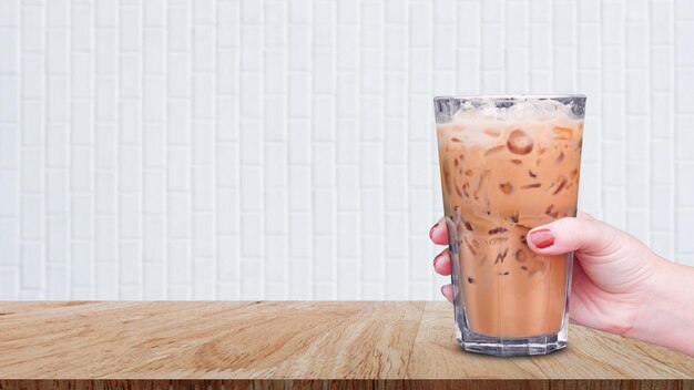 Hand holding the glass iced coffee on wooden table on white background Ice latte coffee