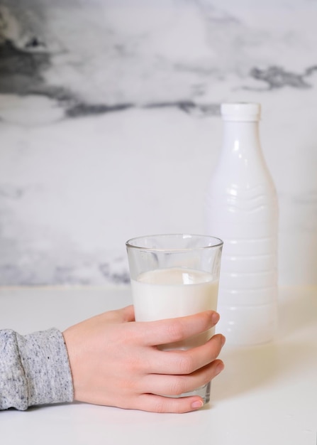 A hand holding a glass of milk next to a bottle of milk