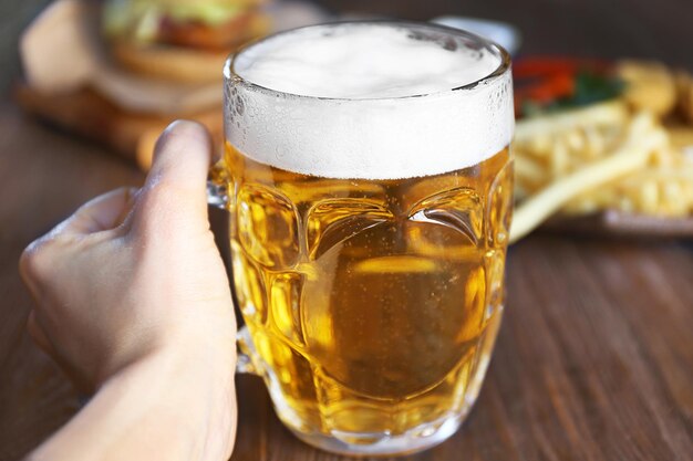 写真 暗い木のテーブルに軽食と軽いビールのガラス ジョッキを持っている手をクローズ アップ