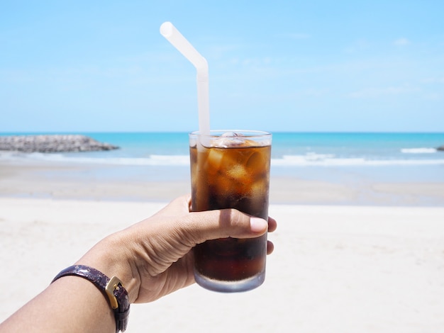 Hand holding glass of soft drink on beach.