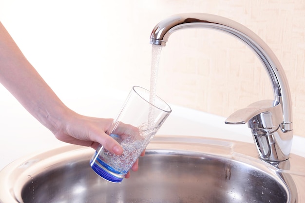 Foto mano che tiene un bicchiere d'acqua versato dal rubinetto della cucina