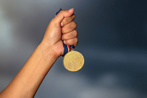 Hand holding gold medal on against cloudy sky 