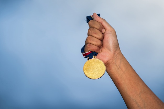 Photo hand holding gold medal on against cloudy sky