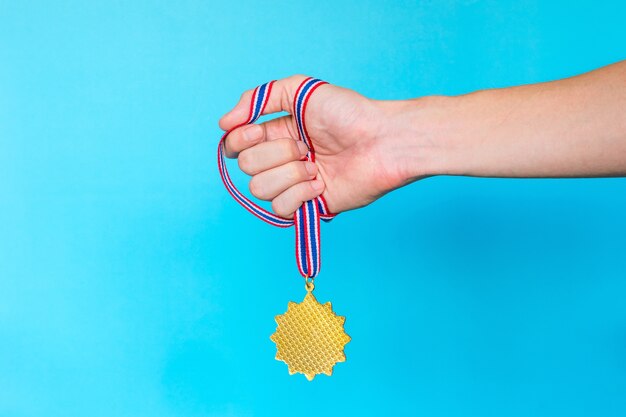 Photo hand holding gold medal with ribbon on blue background.