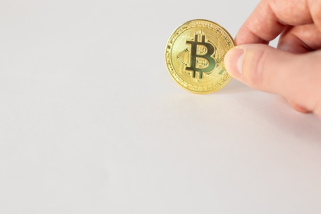 Hand holding a golden bitcoin isolated on white wall