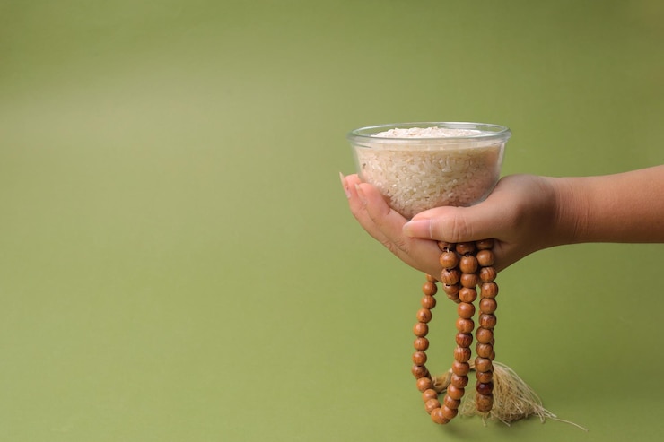 Photo hand holding grain rice bowl with tasbih on sage background with copy space for zakat concept on ram
