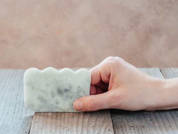 Hand holding a green jade guasha massage scraper used for facial massage