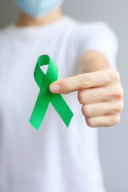 Hand holding green Ribbon for Liver, Gallbladders, bile duct, cervical, kidney Cancer and Lymphoma Awareness month. Healthcare and world cancer day concept