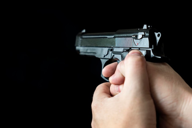 Hand holding a gun on black background concept of the crime of banditry A dangerous shooter and a black pistol on a dark background The hired killer is preparing to shoot