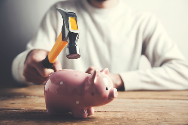 A hand holding a hammer and piggy bank