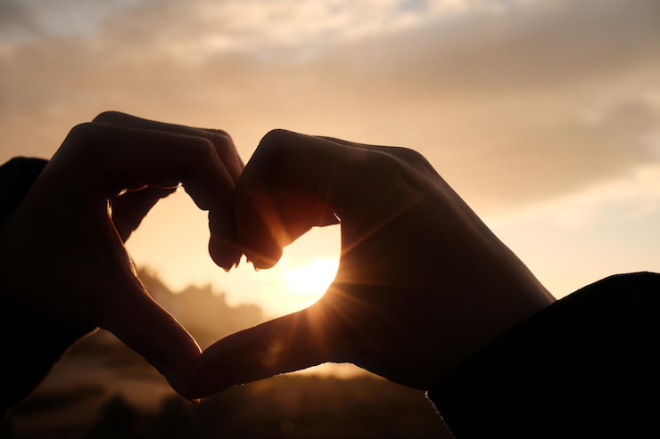 Photo hand holding heart shape against sky during sunset