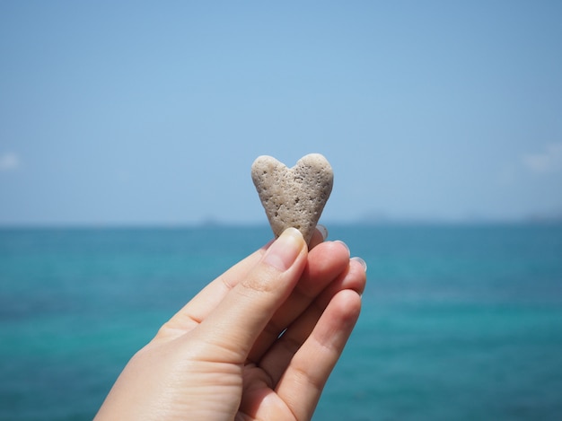 Hand holding heart shape stone over summer beach background