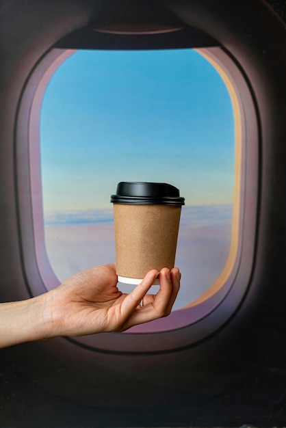 рука держит горячий кофе в стакане на вынос на фоне окна самолета