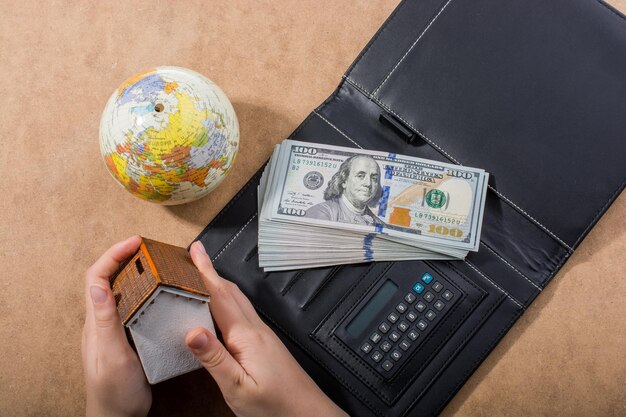 Photo hand holding house beside american dollar banknotes and globe