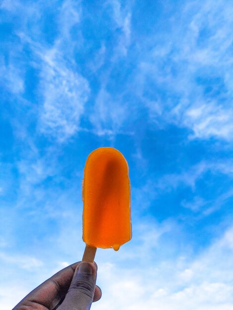 Hand holding ice cream against sky