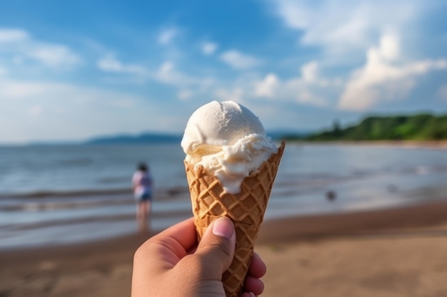 A hand holding a ice cream cone on a beach