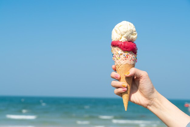 hand holding ice cream cone with blue sky background and copy space