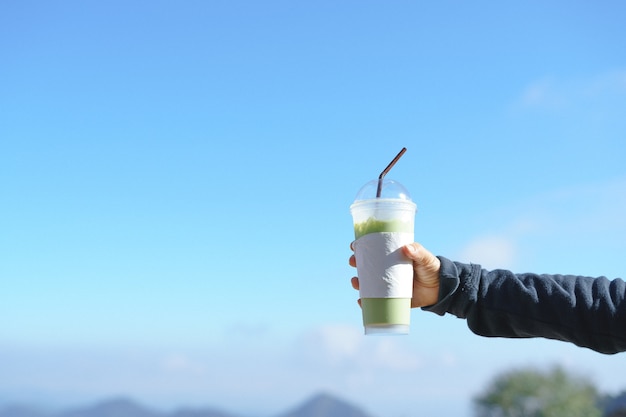 氷の緑茶の杯を手に