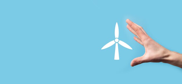 Hand holding an icon of a windmill that produces environmental energy on blue surface