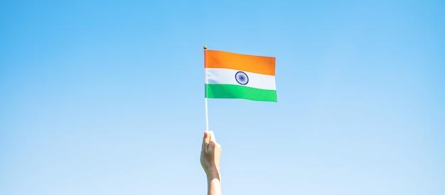 Hand holding India flag on blue sky background. Holiday of India republic Day, happy Independence day and Gandhi Jayanti concepts