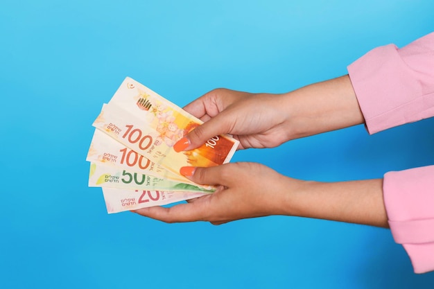 Hand holding israel shekels currency over blue background