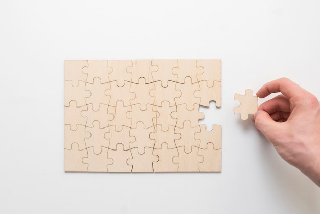 A hand holding a jigsaw piece and complete puzzle on the table