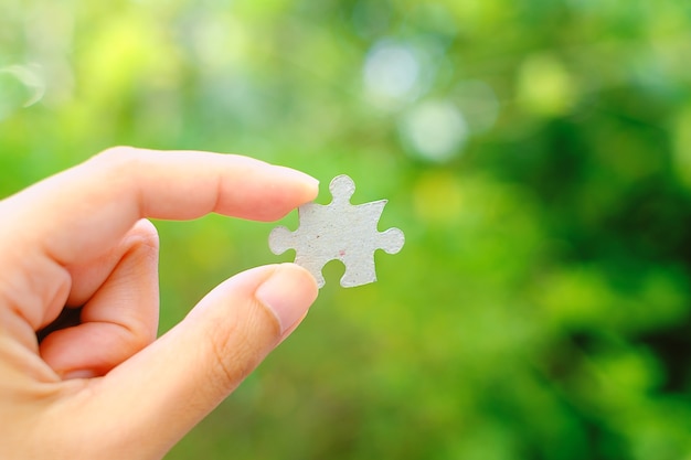Hand holding Jigsaw with blurred green natural background
