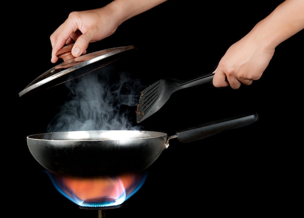 Foto mano che regge una spatola da cucina e padella sul bruciatore