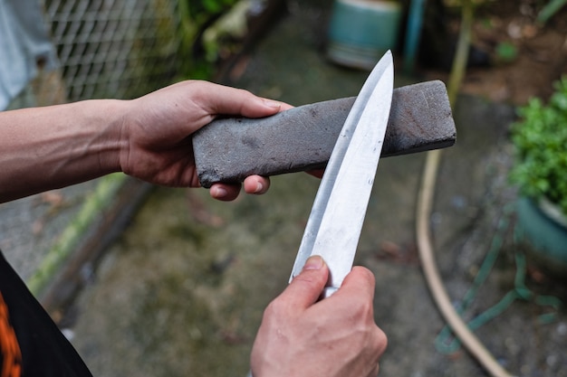 Рука держа нож и точильный камень, чтобы придать форму ножу. Ручная заточка ножа.