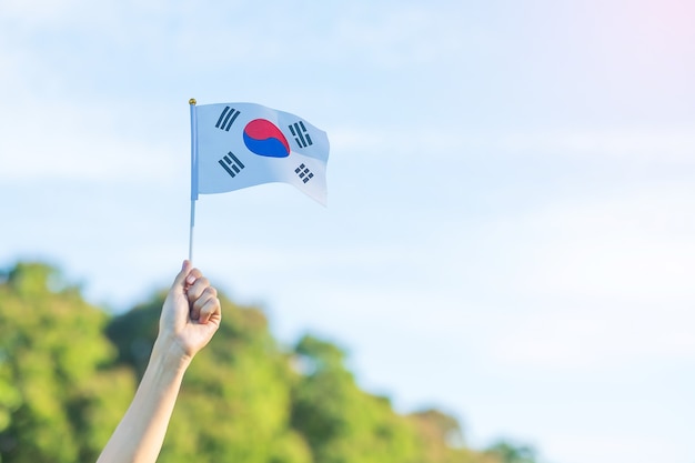 사진 자연 배경에 한국 국기를 들고 손입니다. 건국, 개천절, 공휴일, 광복절 및 행복한 축하 컨셉