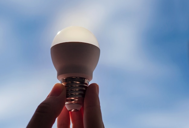 Hand holding led lamp against blue sky