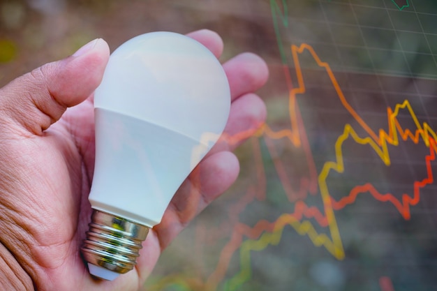 Hand holding a LED light bulb lightemitting diodes In the background graph of the stock exchange