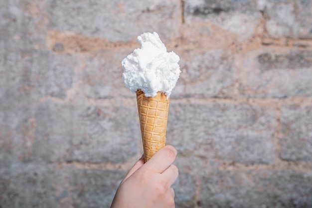 A Hand holding lemon flavored artisan ice cream. Lemon ice cream served in a waffle cone. Home made ice cream