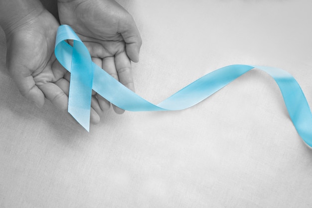 Hand holding Light blue color ribbon on white isolated background with copy space. Lymphedema and Prostate Cancer Awareness month symbol. Healthcare medical and insurance concept. Male cancer.