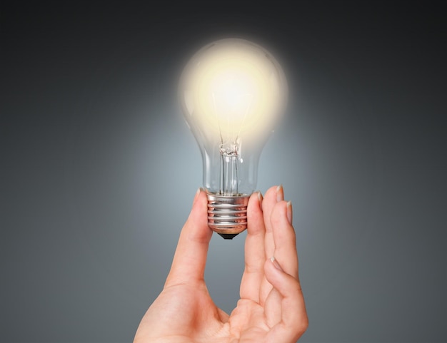 Hand holding light bulb on gray background