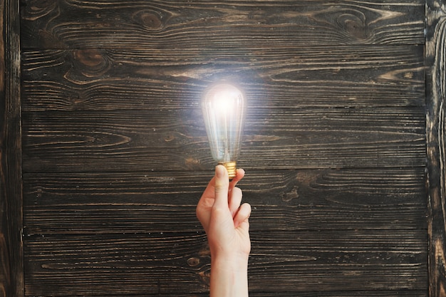 Hand holding light bulb on wooden board