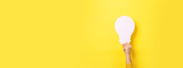 Hand holding light bulb over yellow background, panoramic layout