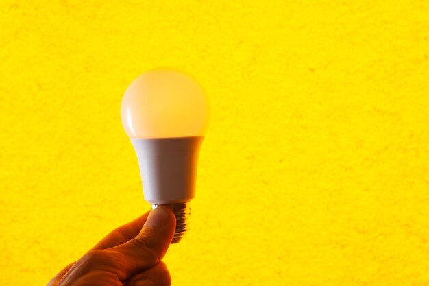 Hand holding a light bulb on a yellow background