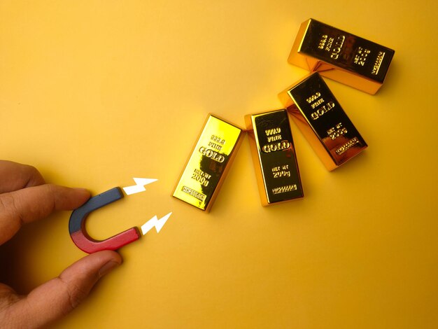 Hand holding magnet attract the gold bar on a yellow background