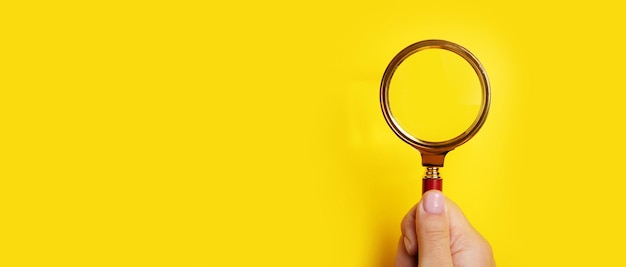 Hand holding magnifier over yellow background, search concept, panoramic layout