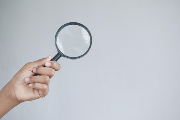 Hand holding magnifying glass against white