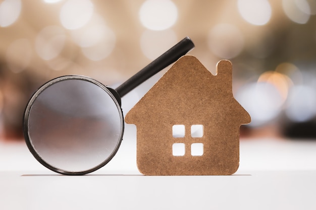 Hand holding magnifying glass and looking at house model