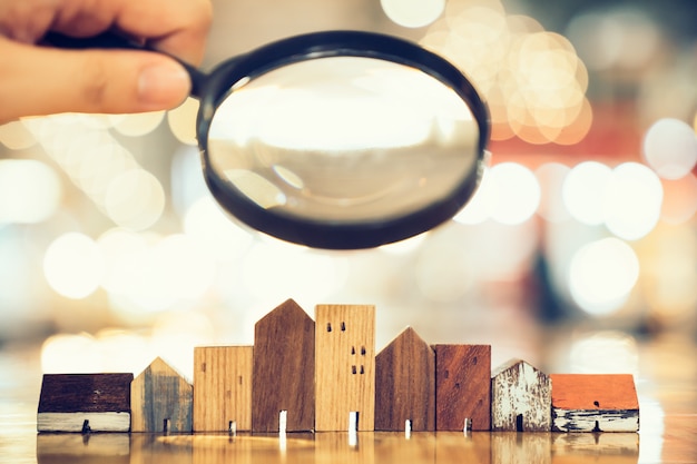 Hand holding magnifying glass and looking at house model