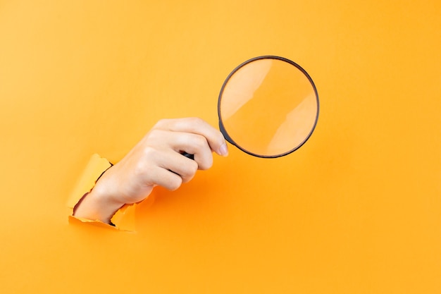 Hand holding magnifying glass protruding from wall