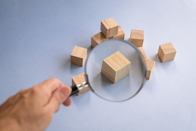 Hand holding a magnifying glass over wooden block