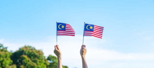 Hand holding malaysia flag on blue sky background. september\
malaysia national day and august independence day