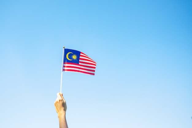 Mano che tiene la bandiera della malesia sul fondo del cielo blu. giornata nazionale della malesia di settembre e giorno dell'indipendenza di agosto