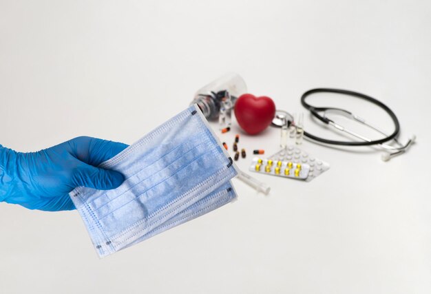 Hand holding a medical mask against the background of a stethoscope and tablets